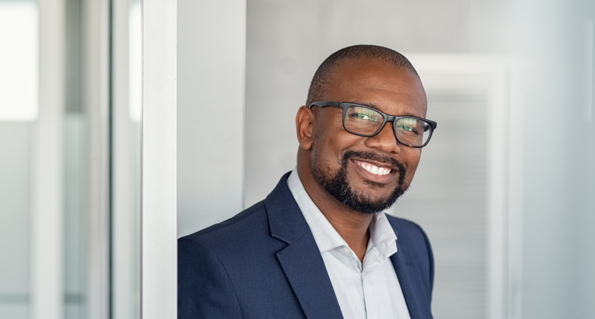 A smiling African American businessman, wearing glasses and a suit, who appears to be a supervisor.