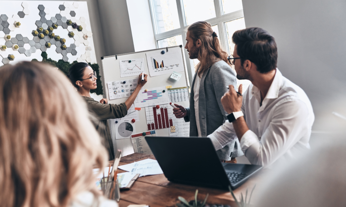 A group of people in discussion around a flipchart with bar charts showing business growth