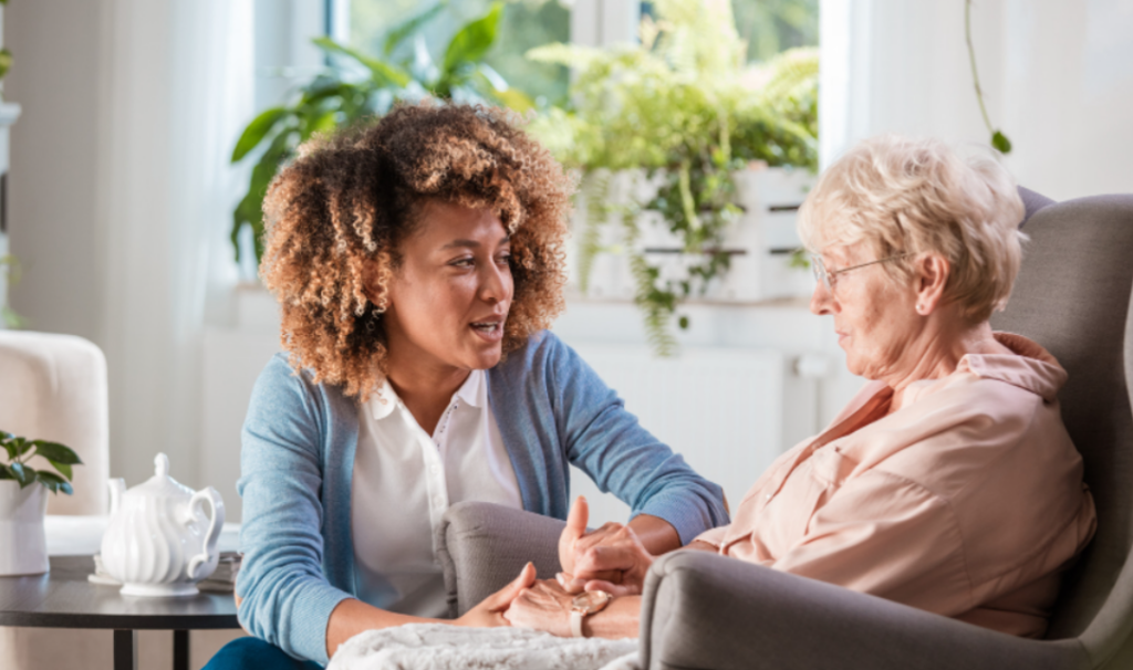 A woman engaging in health and social care, conversing with an older woman in a chair, demonstrating the value of preparing to work in health and social care.