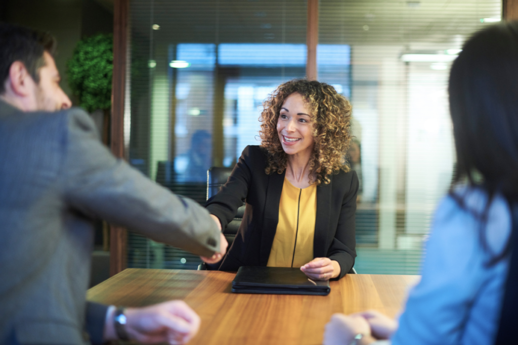 A woman interviewee shaking hands with a potential employer over a desk positively demonstrating qualities employers are looking for