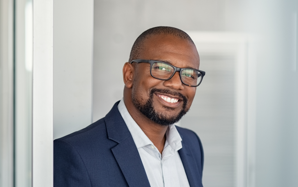 A smiling businessman, wearing glasses and a suit, who appears to be in a position of management after the Introduction to Management course.