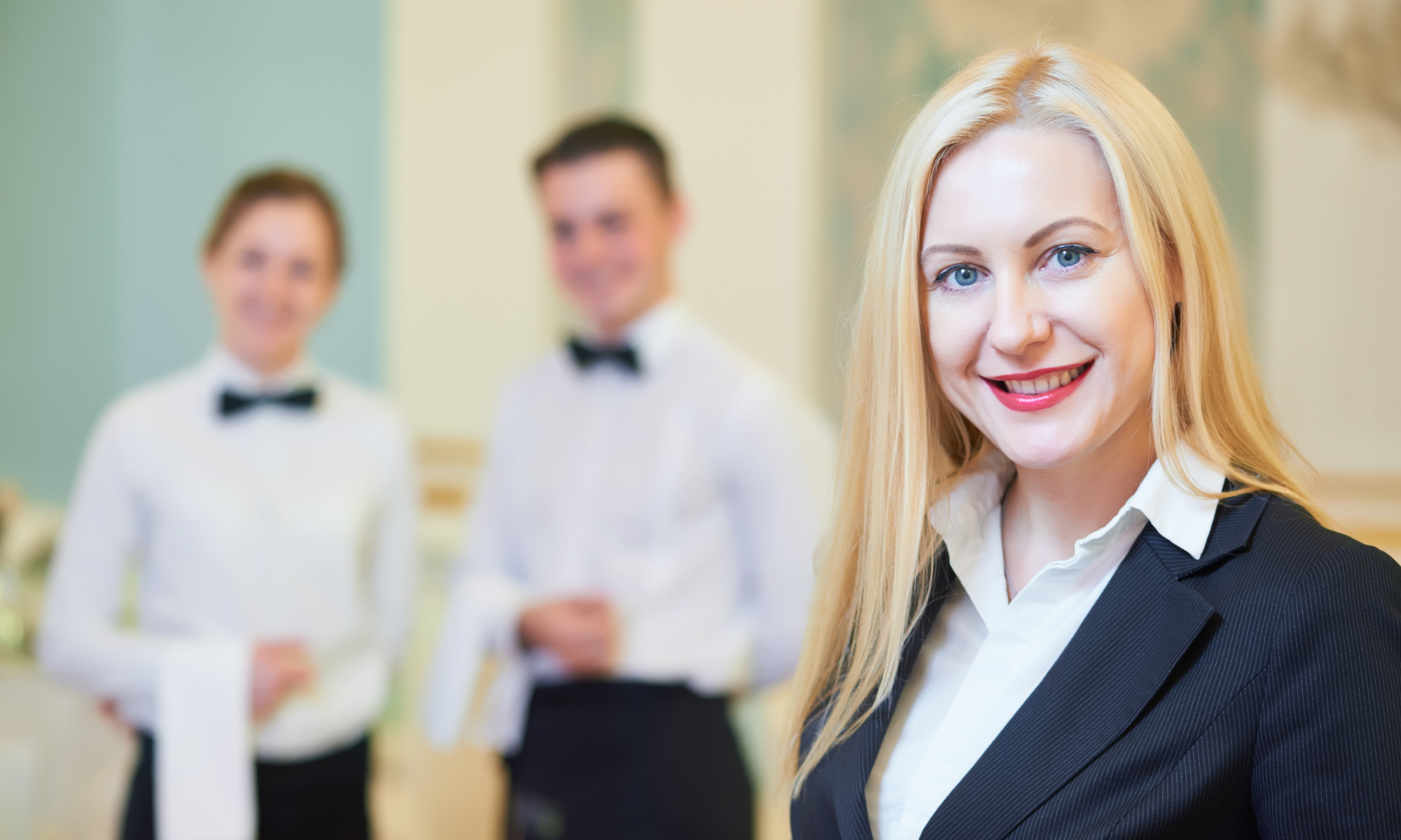 Smartly dressed female hospitality manager with two male staff in uniform in the background, illustrating the Hospitality Supervision and Leadership Principles Level 3 award.