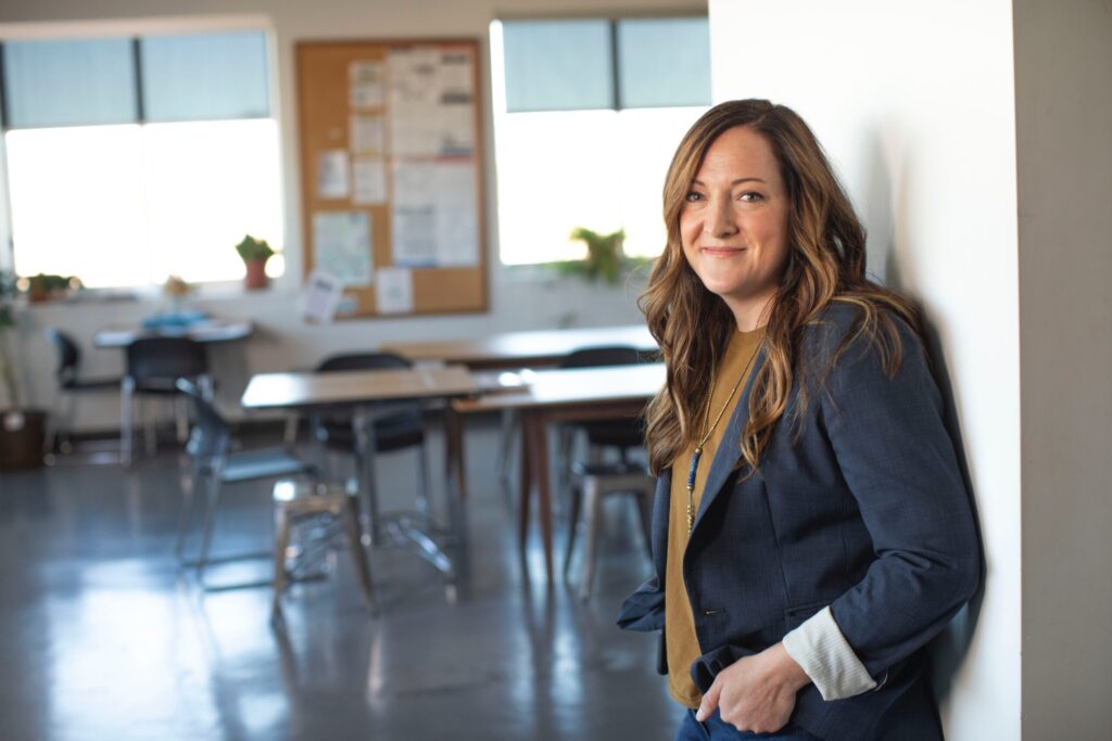 Support Work in Schools Level 2 Award. A smiling woman leaning against a wall in a classroom.