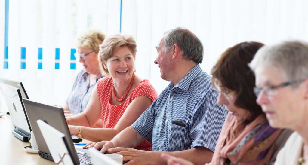 Microsoft PowerPoint for Beginners - for A group of people sitting at a table, learning digital skills with laptops.