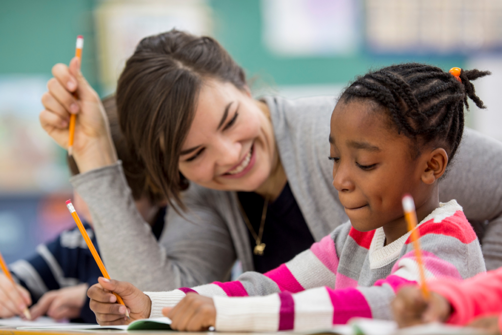 A young woman happily teaching a child and helping with their development showing the value of the Introduction to Phonics and Exploring Writing with the Under-5s courses.